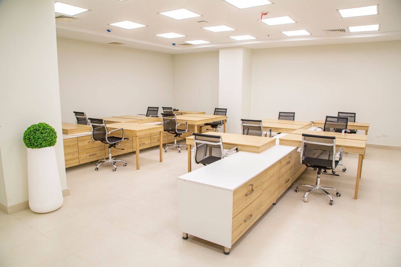 A bright, modern office space featuring wooden desks, rolling chairs, and ample lighting.